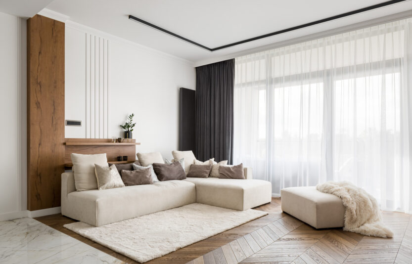 Elegant and comfortable designed living room with big corner sofa, wooden floor and big windows